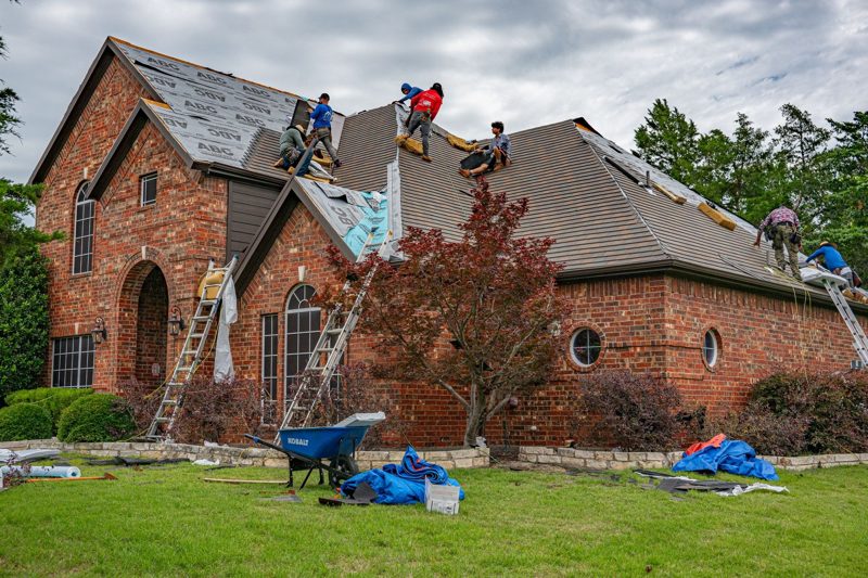 Roofing crew tearing off old shingles during a roof replacement in Kansas City, MO